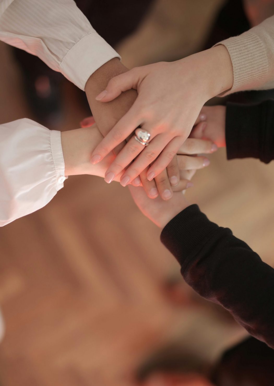 pexels-photo-3830752-3830752 Top view of faceless friends in different clothes stacking hands together while standing on wooden floor indoor on sunny day
